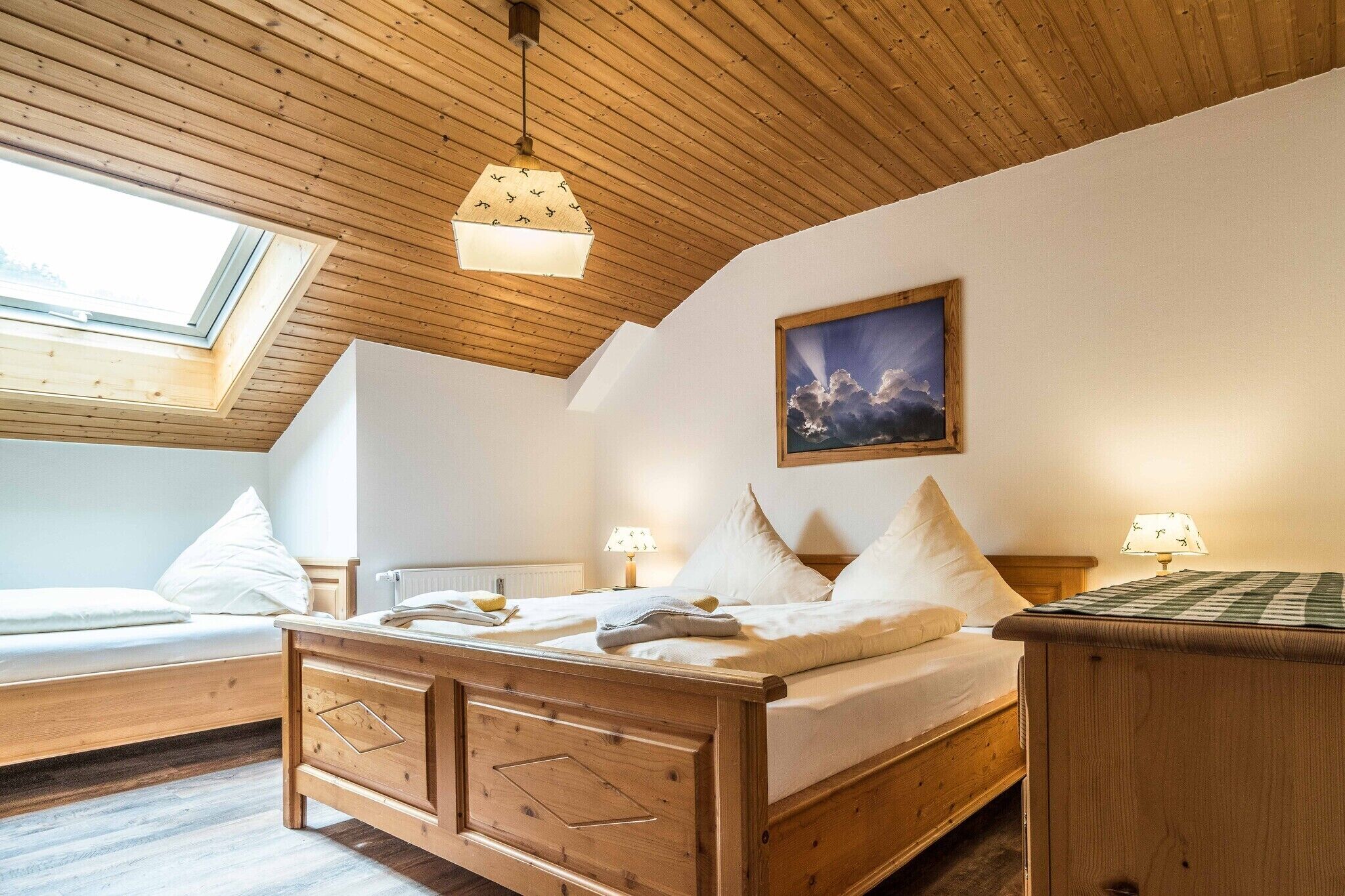 Ein Schlafzimmer mit Holzbalkendecke, einem Oberlicht, einem Bett mit weißen Leinen, einem Nachttisch mit Lampe und einem Gemälde an der Wand.