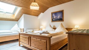 Un dormitorio con techo de madera, un tragaluz, una cama con ropa blanca, una mesita de noche con lámpara y un cuadro en la pared.