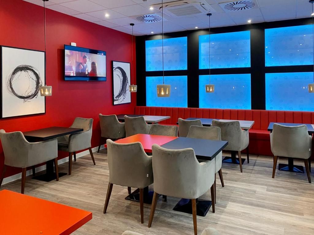 A restaurant interior with red walls, multiple tables and chairs, a television, and large windows with blue-tinted glass.