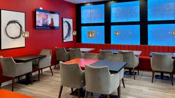 A restaurant interior with red walls, multiple tables and chairs, a television, and large windows with blue-tinted glass.