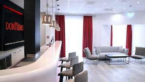 Un moderno vestíbulo de hotel con una recepción, zona de estar y un amplio ventanal con cortinas rojas.