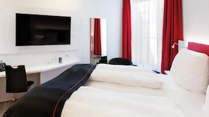 Habitación de hotel con cama, escritorio, silla, televisión y cortinas rojas.