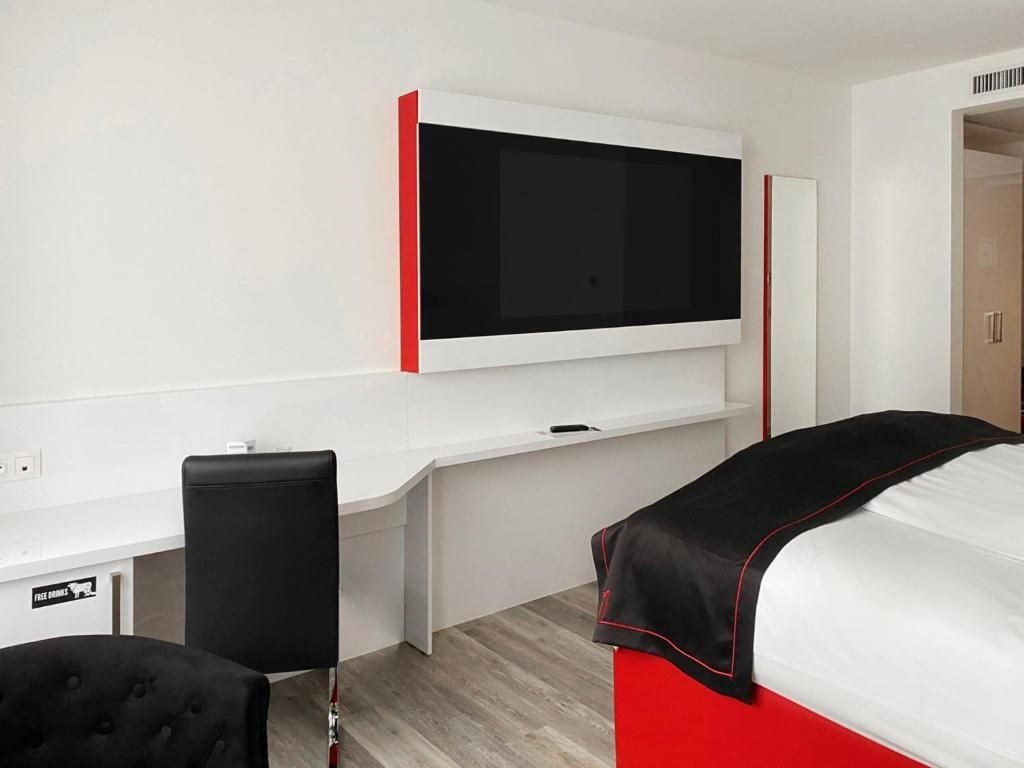 A hotel room with a bed, a desk, a chair, and a television mounted on the wall.