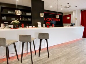 A reception area with a counter, bar stools, a sign reading "DORMERO", and a red curtain. - Dormero Hotel Darmstadt (Darmstadt)