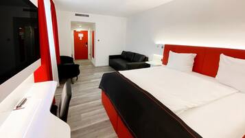 A modern hotel room with a large bed, a desk, a chair, and a sofa.