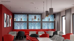 Interior moderno de restaurante con asientos rojos y grises, ventanas amplias con un diseño texturizado e iluminación colgante contemporánea.