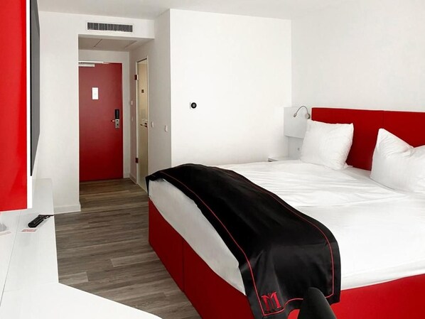 Habitación de hotel con cama, escritorio y pared roja.