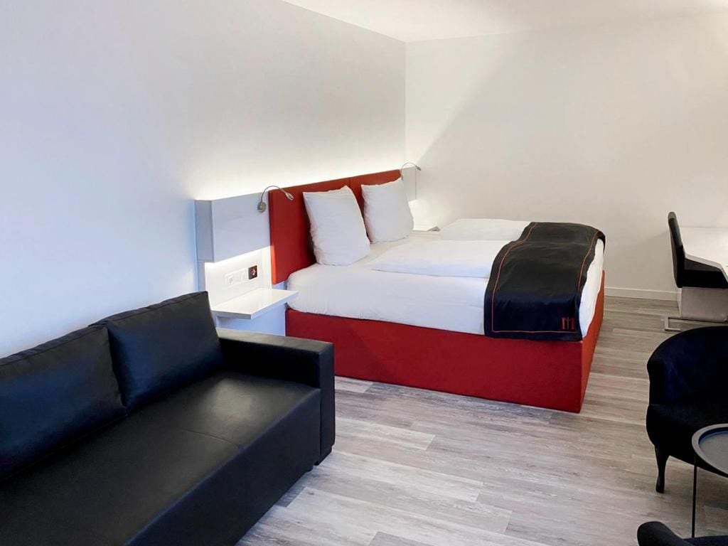 A modern hotel room with a bed, a black sofa, a small table, and a chair.
