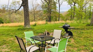 An outdoor dining area with a table and chairs, a grill, and a natural backdrop. - Tiny House close to Buffalo Point (Saint Joe)