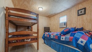 A bunk bed with a quilted bedspread and pillows, a television, and a window with blinds. - Tiny House close to Buffalo Point (Saint Joe)