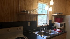 A kitchen with wooden cabinets, a black countertop, a stainless steel sink, a white stove, and a window with a view of greenery outside. - Tiny House close to Buffalo Point (Saint Joe)