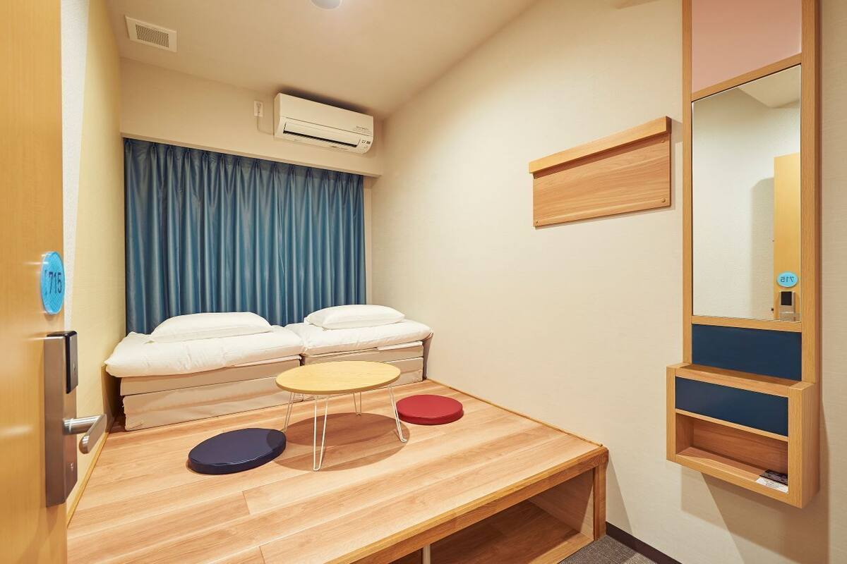Ein Hotelzimmer mit einem Bett, einem kleinen Tisch, zwei Hocker, einem Spiegel und einer Klimaanlage.