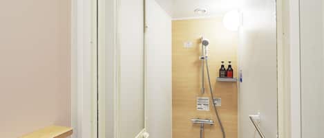 Box chuveiro estreito com porta de madeira, chuveiro manual, torneira fixada na parede e duas embalagens de shampoo e condicionador numa prateleira.