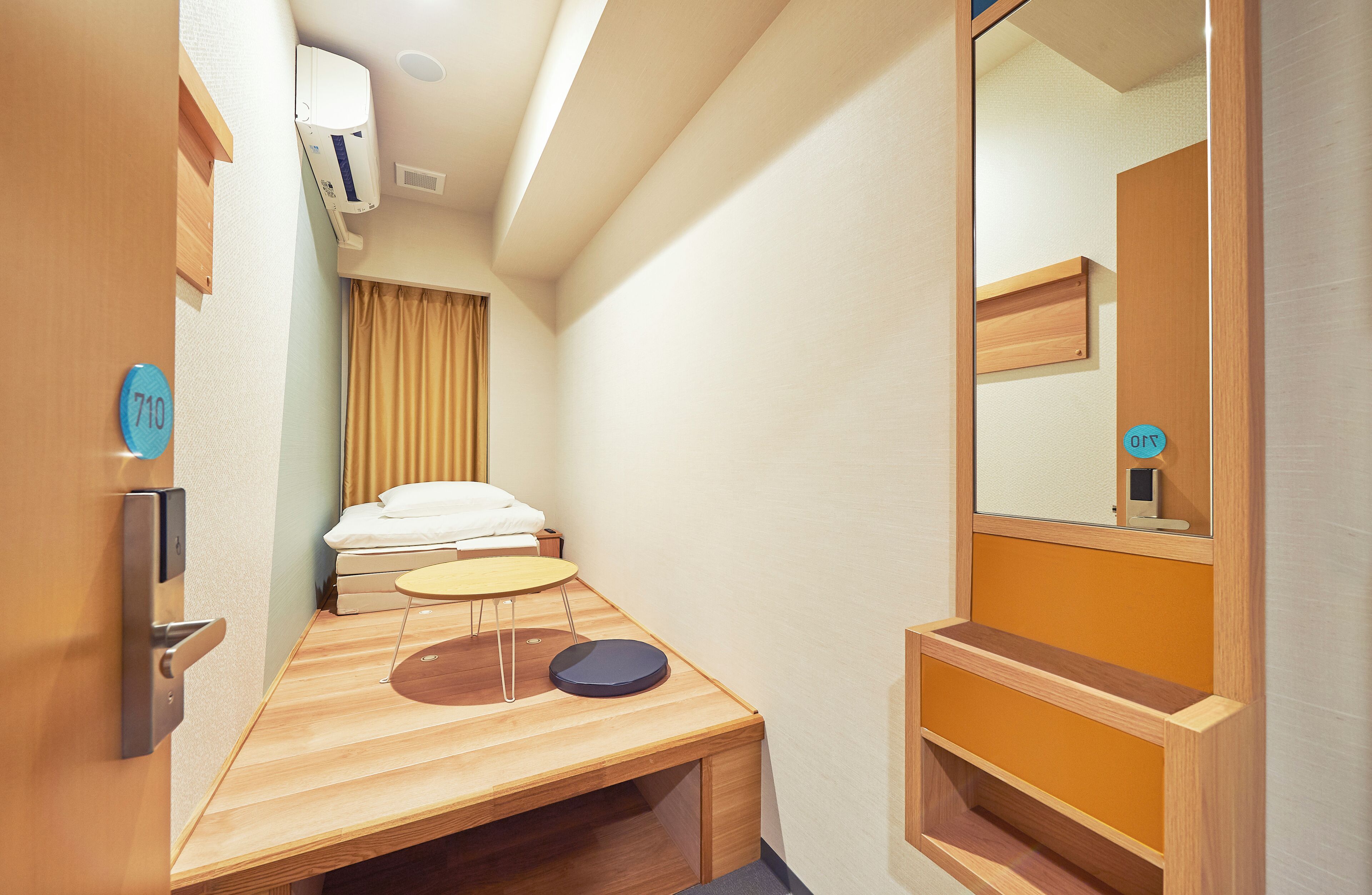 Een kleine hotelkamer met een bed, een tafeltje, een spiegel en een houten bank.