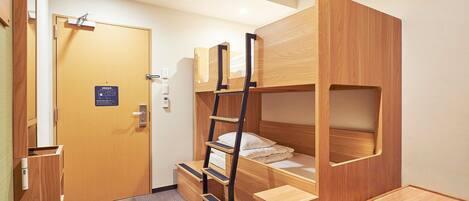 A compact room with a bunk bed, a small desk, and a chair. There is a door with a sign, a light switch, and a thermostat on the wall.