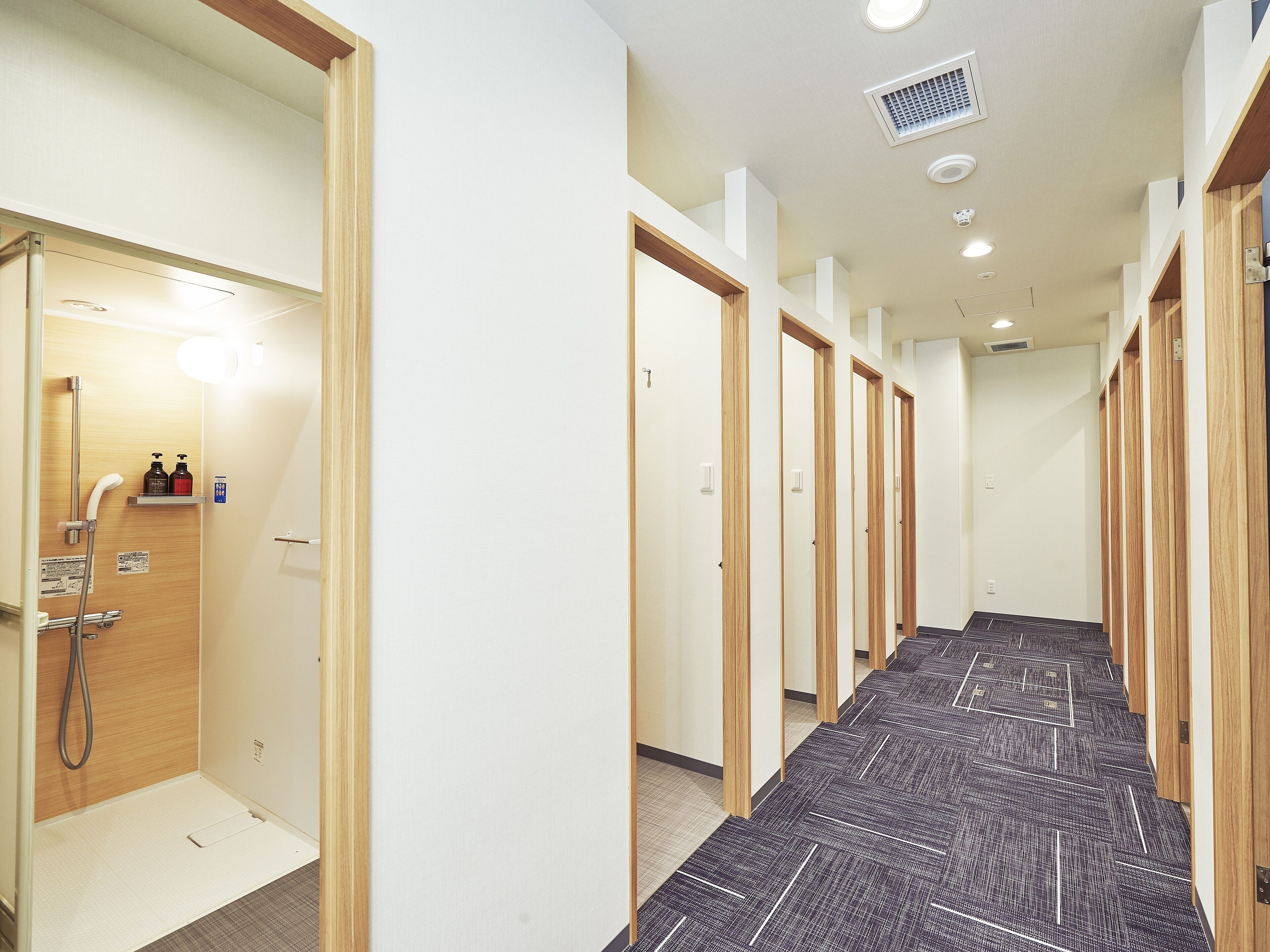 A hotel corridor with wooden doors, a shower area, and a patterned carpet.