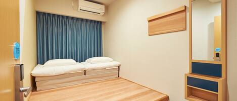 A compact bedroom with a single bed, a wooden nightstand, a wall-mounted shelf, and a ceiling-mounted air conditioner.