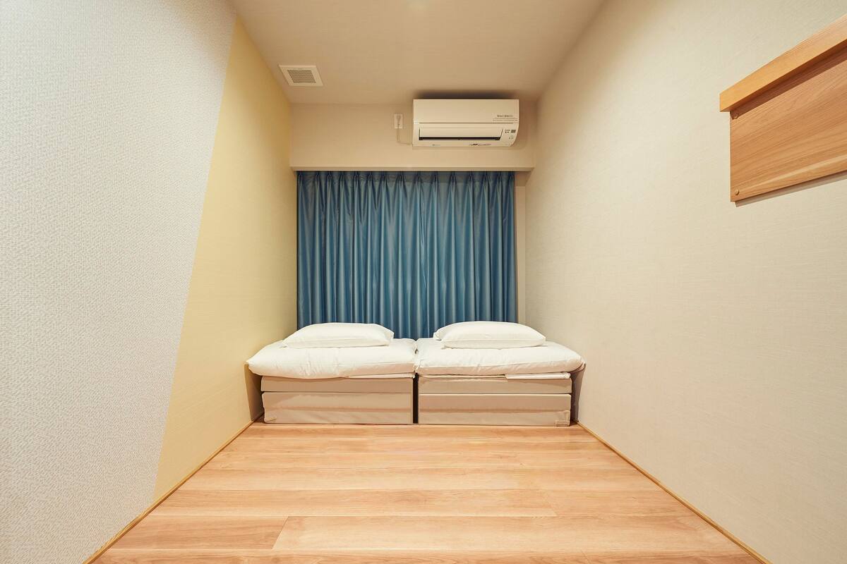 Eine kleine Einzimmerwohnung mit Bett, einer Klimaanlage und einem Fenster mit blauen Vorhängen.
