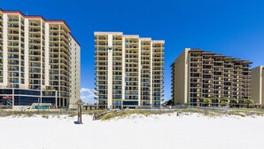 Un hôtel en bord de mer, composé de plusieurs immeubles de grande hauteur, avec une plage de sable en premier plan et un ciel bleu dégagé.