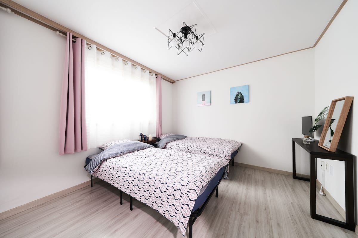 A bedroom with two beds, a ceiling light fixture, and a bedside table with a mirror and a plant.