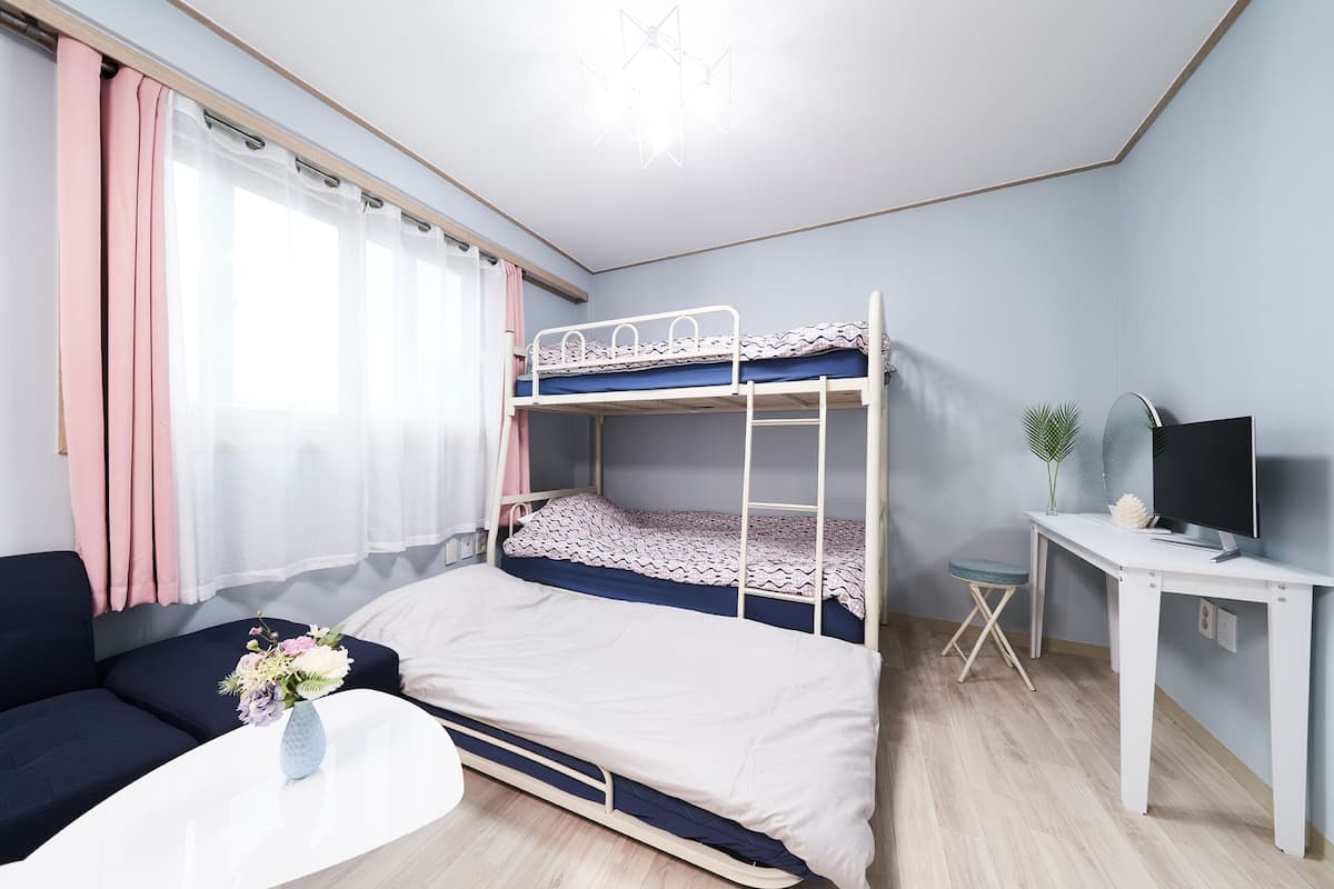 A bunk bed with a desk and a TV, a sofa, and a small table with a vase of flowers.