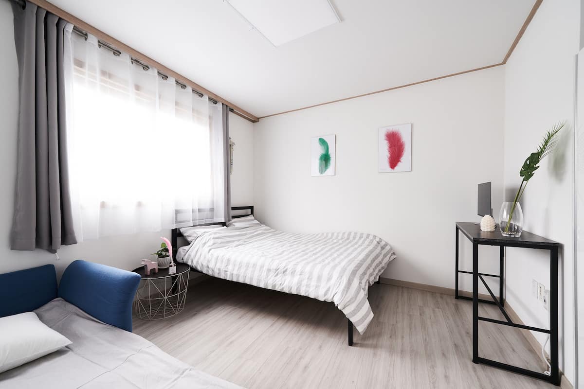 A modern bedroom with a bed, a blue sofa, a small side table, and a bedside table with a vase.