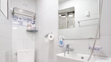 A bathroom with a toilet, sink, mirror, and shower.