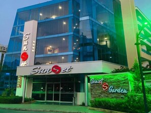 Un edificio moderno con un amplio frente de vidrio y señalización que dice 'Sunset Garden'.