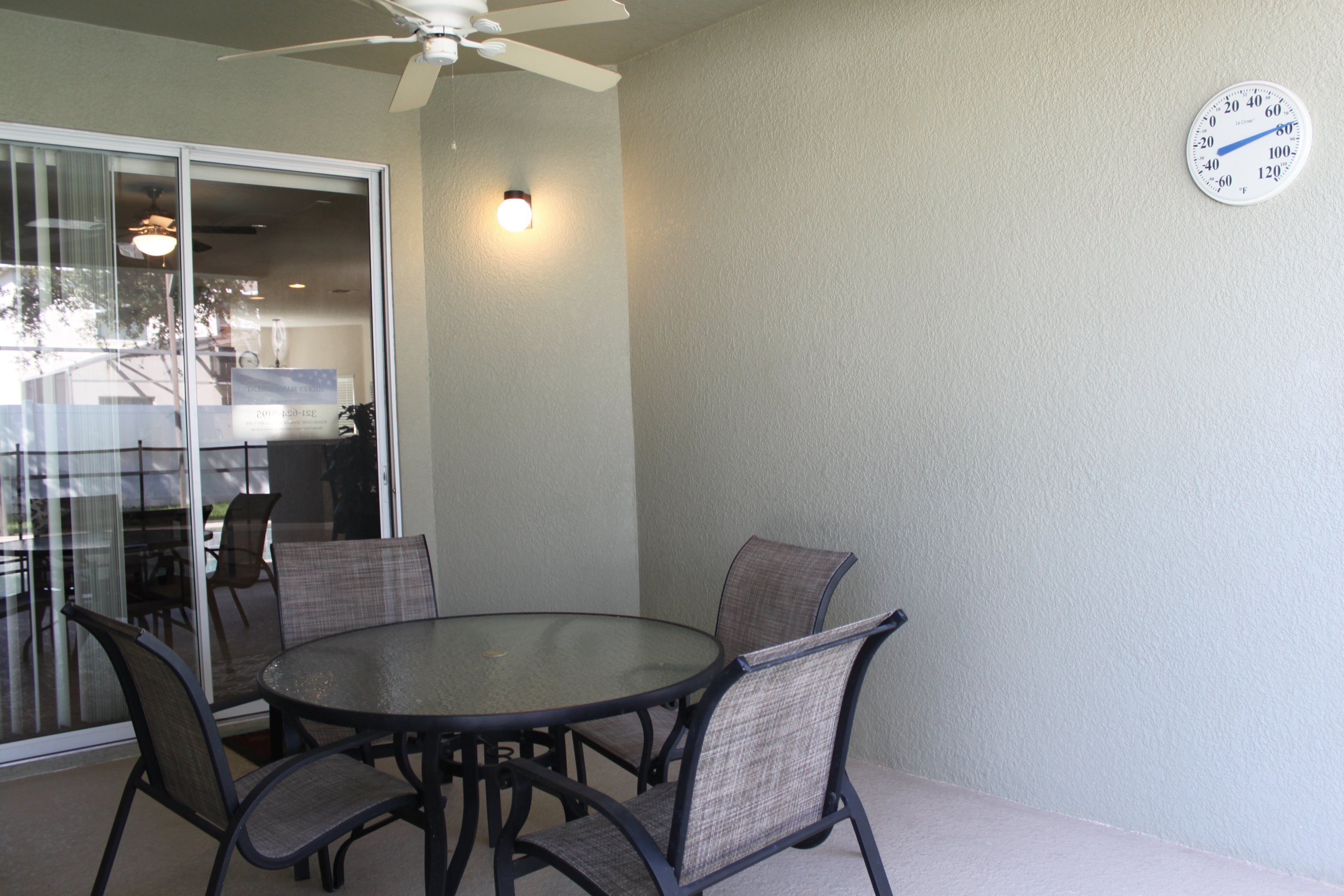 A patio with a round table and chairs, a ceiling fan, and a wall clock.