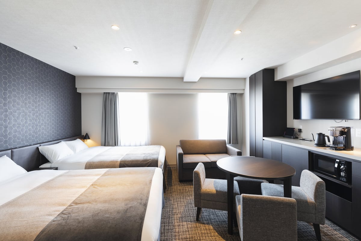 Ein Hotelzimmer mit zwei Betten, einem Schlafsofa, einem Esstisch und einem Fernseher.