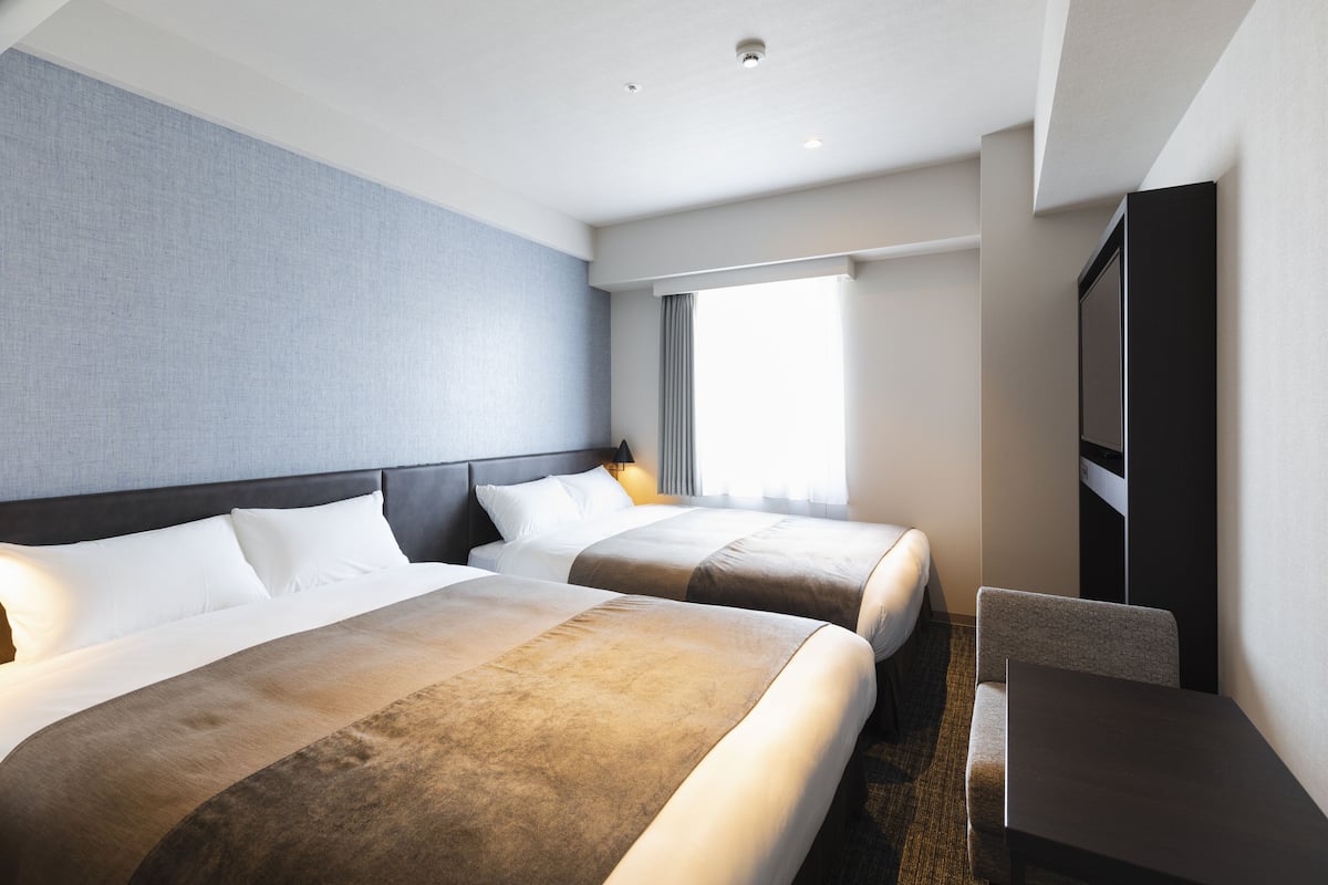 Ein Hotelzimmer mit zwei Betten, einem Schreibtisch und einem Fernseher.