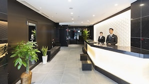Un hall d’hôtel moderne avec un comptoir d’accueil, deux réceptionnistes et des plantes en pot.