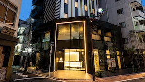 Un immeuble moderne de grande hauteur, doté de fenêtres illuminées, d’une entrée en verre et entouré d’un environnement urbain.