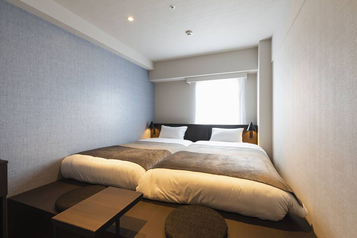 Ein modernes Hotelzimmer mit einem großen Bett, einem kleinen Schreibtisch und einem Fenster mit Tageslicht.