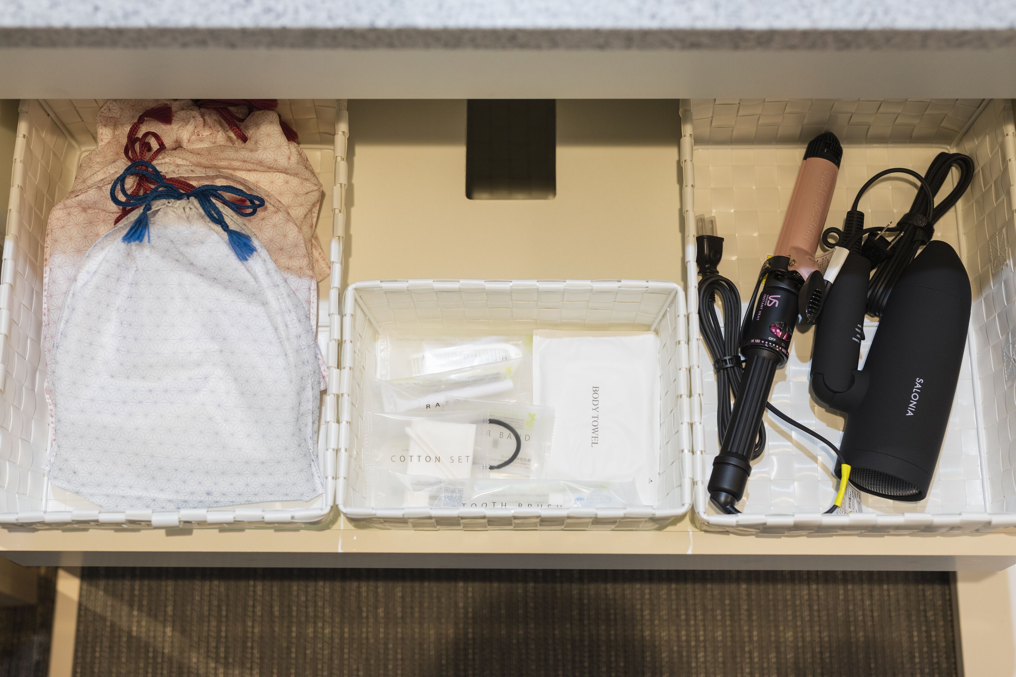 A storage unit with compartments containing a face mask, cotton set, body towel, hairdryer, and other personal items.