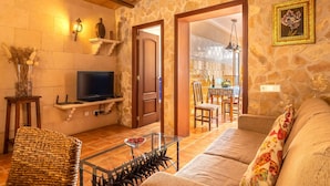 Un salon chaleureux avec un mur en pierre, un téléviseur, un canapé et un coin repas visible à travers une porte ouverte.