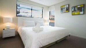 Hotellihuone, jossa on suuri sänky, yöpöytä, lamppu ja ikkuna, josta on näkymä.