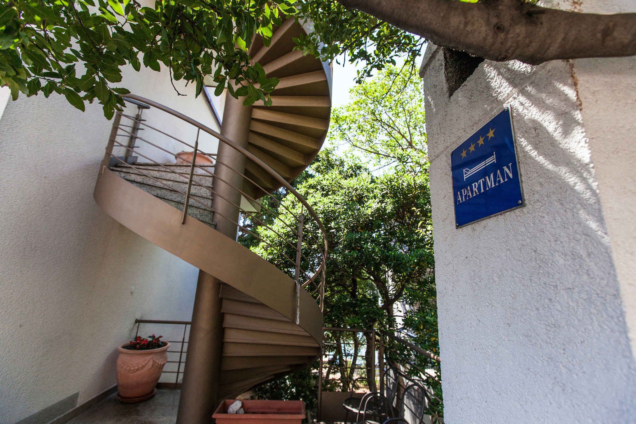 Una escalera de caracol con barandilla metálica, una planta en maceta y un cartel que indica un apartamento.