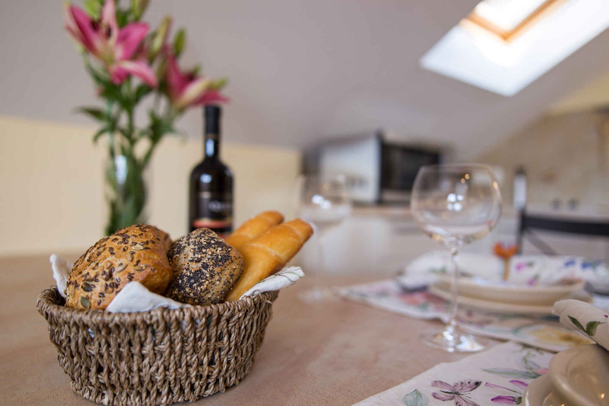 Cesto de vime com vários pães e uma garrafa de vinho sobre uma mesa.