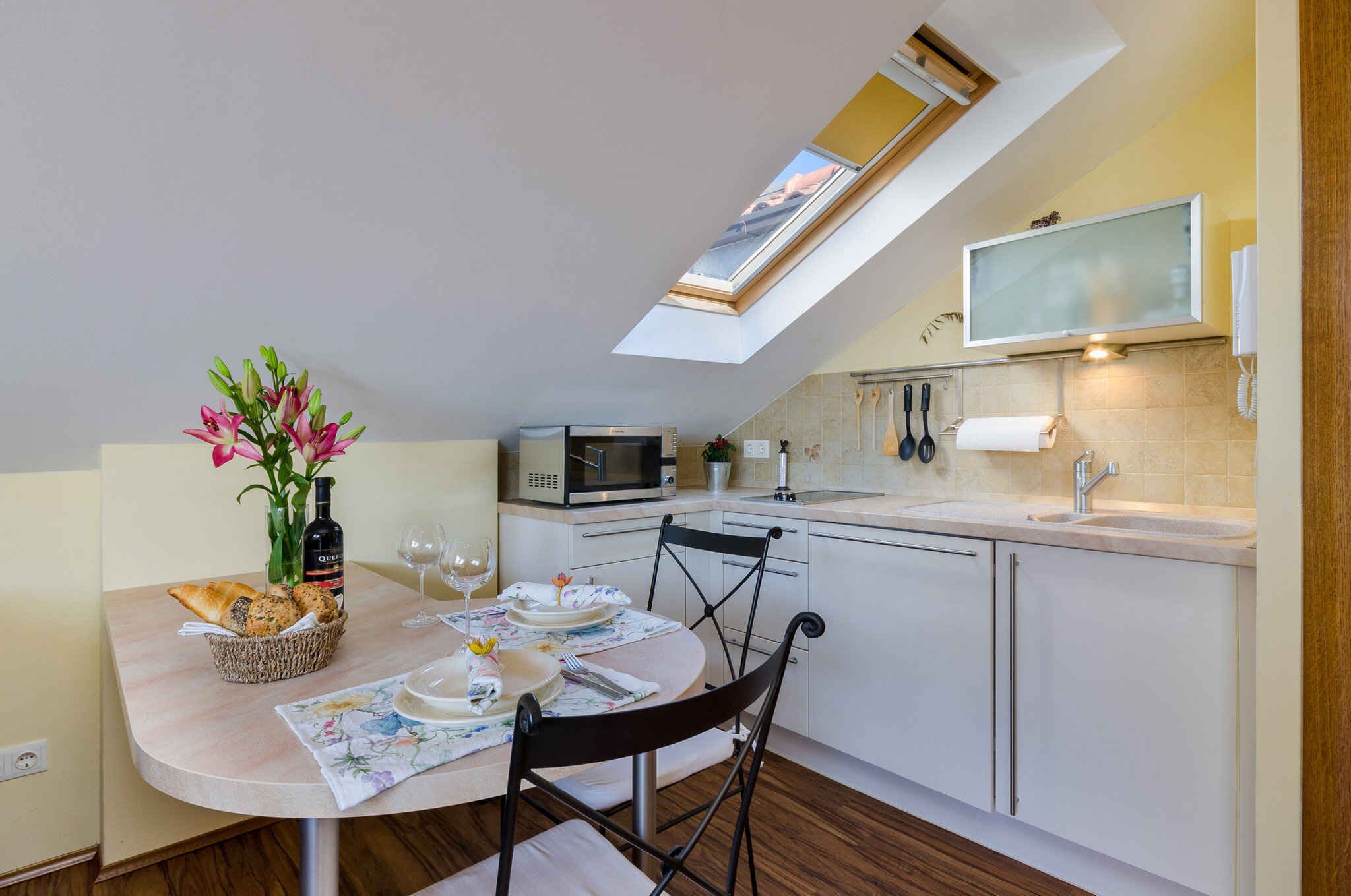 A modern kitchen with a skylight, a microwave, a sink, and a dining area with a table set for two.