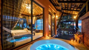 A modern hotel room with a large glass window, a hot tub, and a balcony with a view of the sunset. - Nirvana  Beach Resort (Ko Lanta)