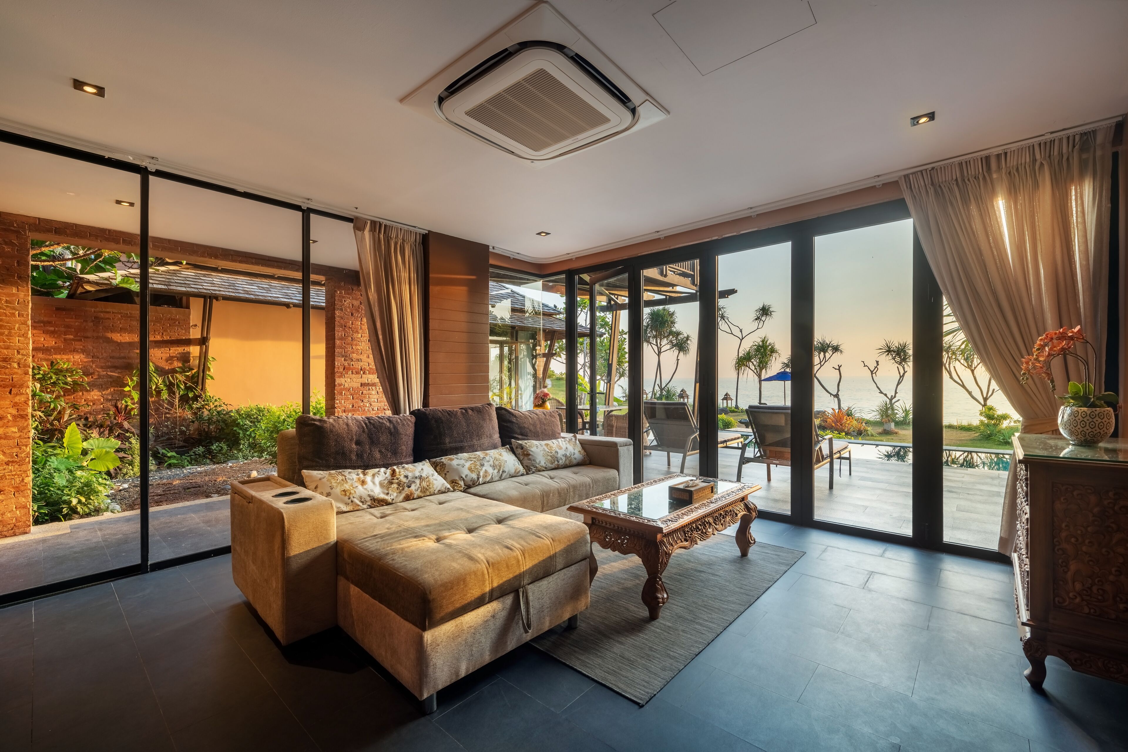 A modern living room with a sectional sofa, a glass coffee table, and a view of a garden through large sliding glass doors.