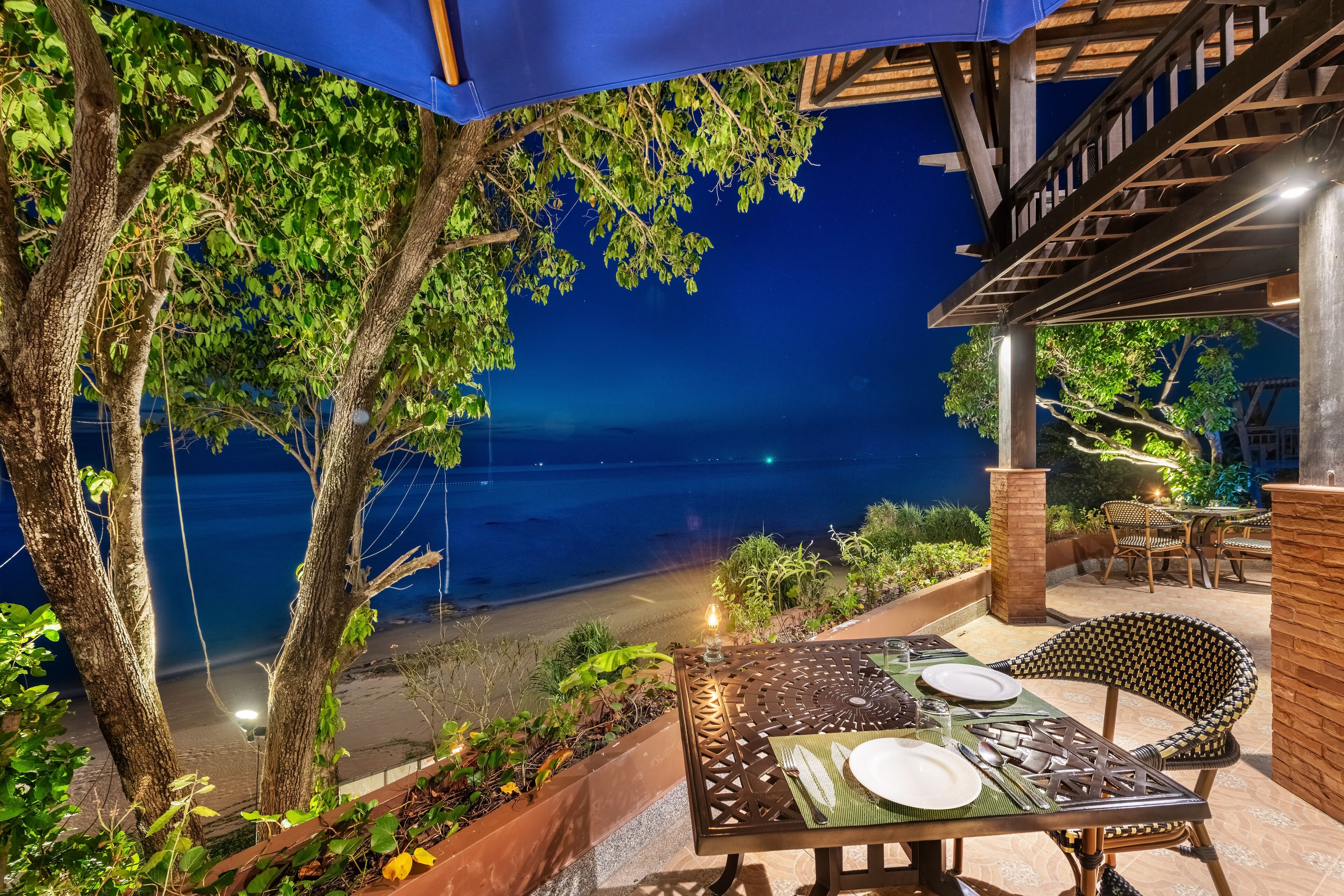 An outdoor dining area with a table set for two, overlooking a beach at night.