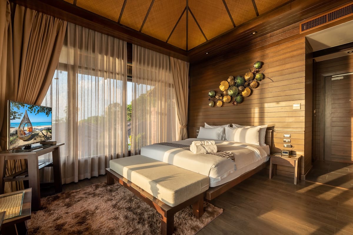 A bedroom with a large bed, a desk with a TV, and a view of the beach.