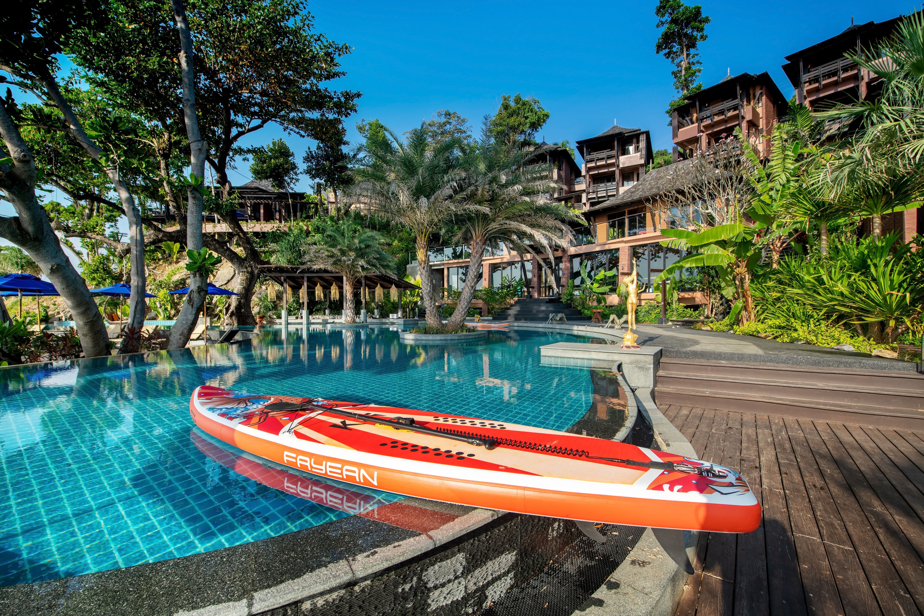 A swimming pool with a red and white kayak, surrounded by tropical plants and wooden walkways.