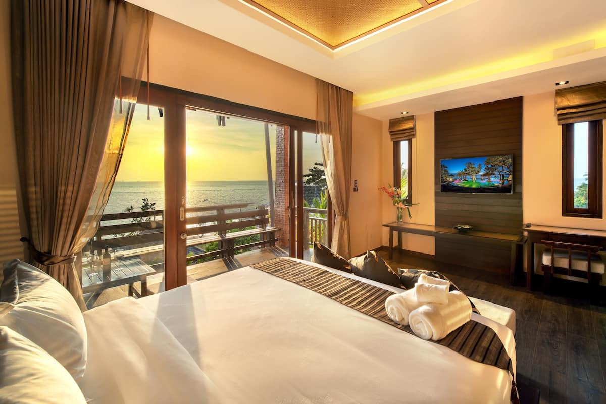 A hotel room with a large bed, a TV, and a balcony with a view of the sea.