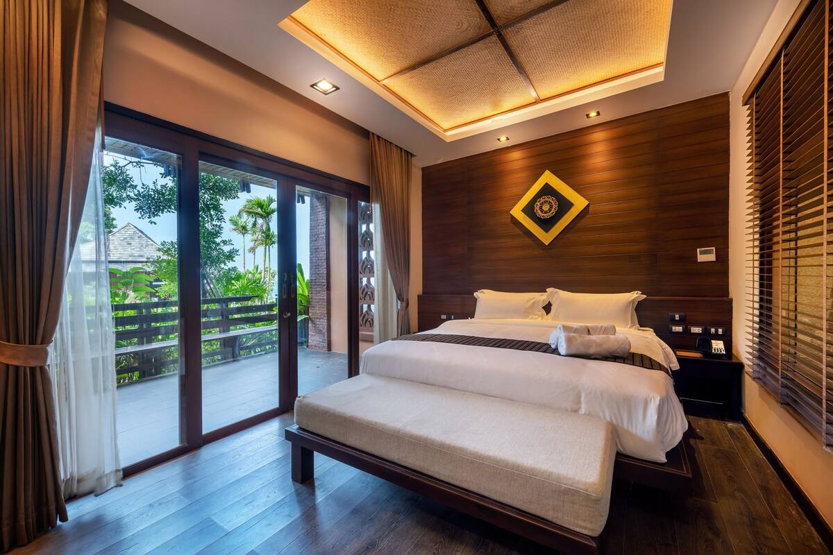 A modern bedroom with a large bed, a bench, and a view of a garden through a sliding door.