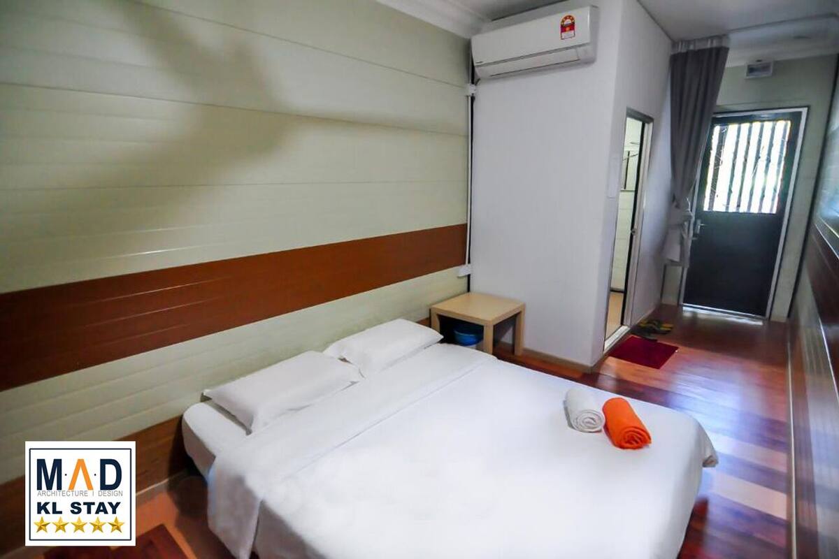 Ein Hotelzimmer mit Bett, Nachttisch, Wand-Klimaanlage und einer Tür mit Vorhang.