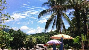 A tropical setting with a clear sky, palm trees, a calm body of water, and a person under an umbrella.
