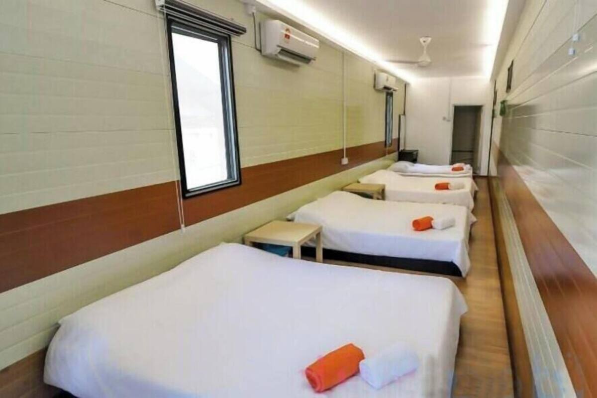 Ein Hotelzimmer mit vier Einzelbetten, jedes mit einem Kopfkissen und einem gerollten Handtuch.